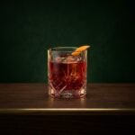 A ruby red Negroni over a large ice cube with a curl of orange peel