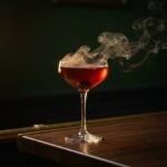 A Smoked Manhattan in a coupe glass with smoke still curling off the surface